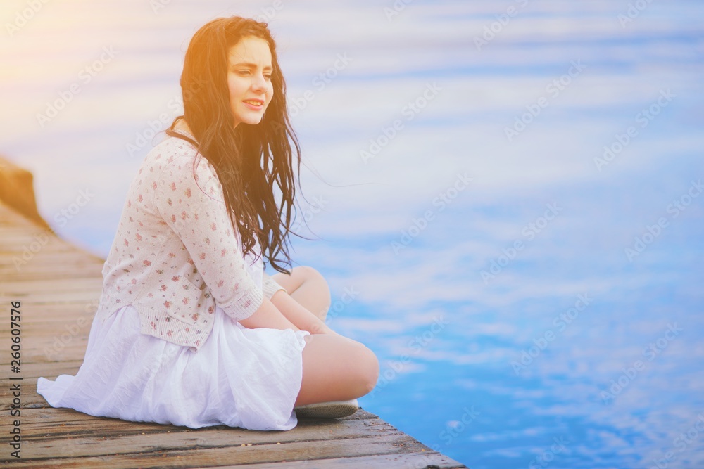 Φωτογραφία Happy young beautiful woman sitting on the pier, smiling, relax and listen silence on sunset in summer sunny day