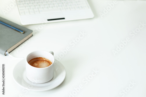 Coffee cup   laptop and grey notpad on white table. Selective focus.