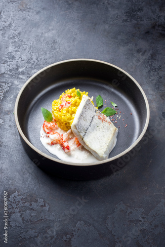 Gebratenes Schellfisch Filet mit Safran Reis und Krabben in Krebs Sauce als closeup auf einer Modern Design Schale mit Textfreiraum 