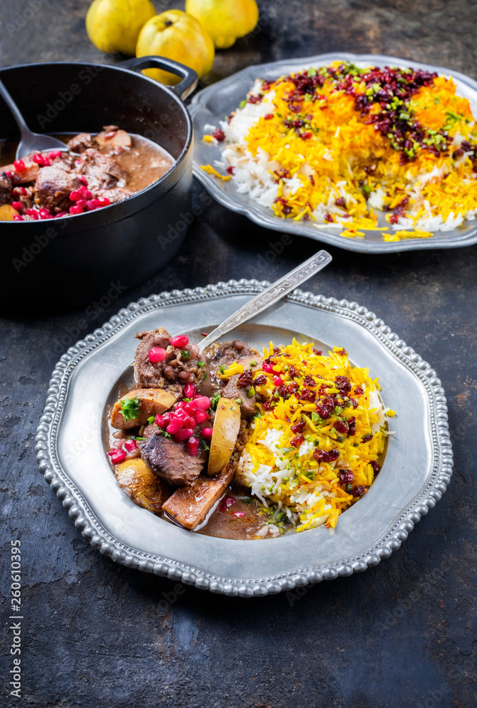 Traditional Iranian khoresh beh stew with chunks of lamb, quinces and saffron rice as closeup in a cast-iron roasting dish and pewter plate