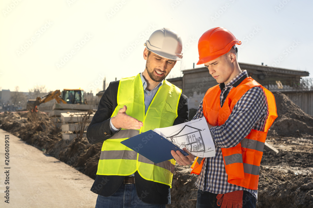 two men are builders workers are engineers at a construction site are looking at the drawings in helmets two men are builders workers are engineers at a construction site are looking at the drawings in helmets