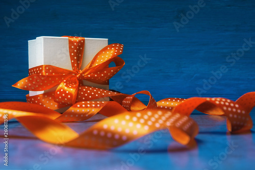 Gift box with spotted orange ribbon against blue background