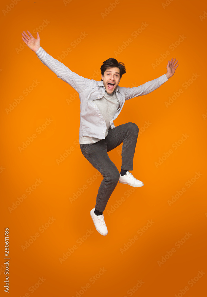 Funny man jumping with raised arms over orange background