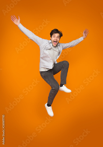 Funny man jumping with raised arms over orange background