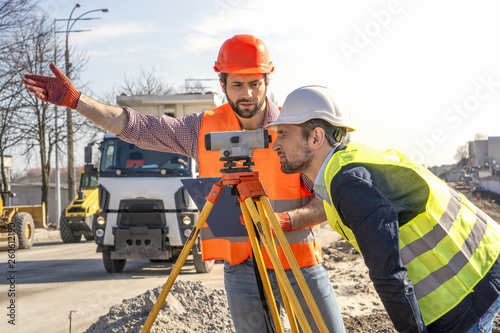 two male surveyor engineer with a device working on a construction site in a helmet