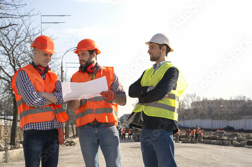 male builders workers engineers at a construction site looking drawings in helmets