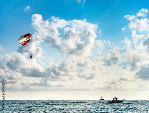 Silhouette of people on a parachute flying behind a motorboat on a holiday by the sea against the blue sky with clouds © maxoidos