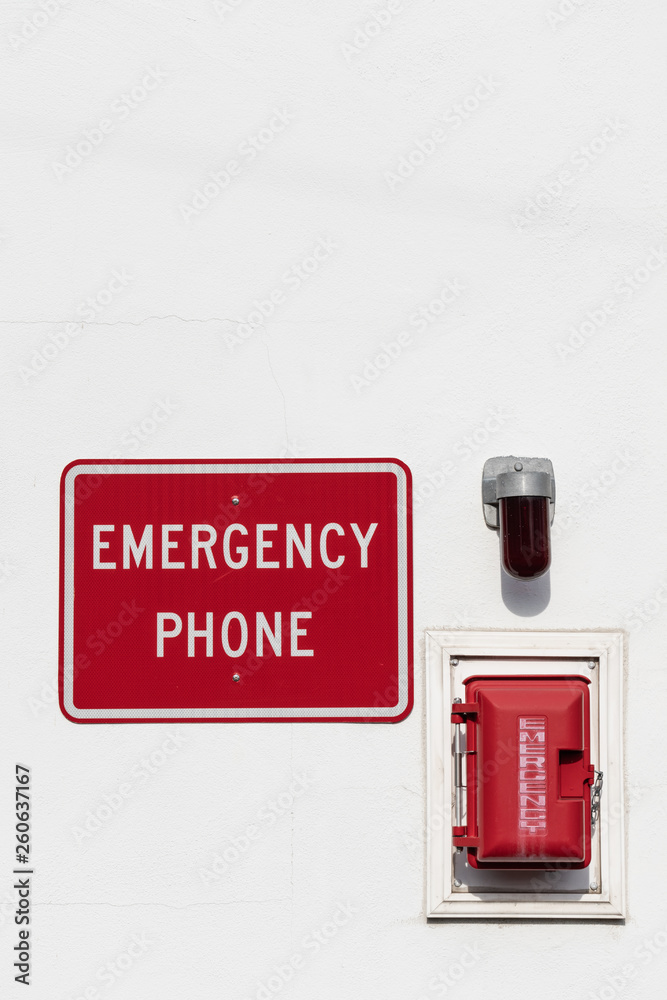 red emergency phone box on white wall with light and sign above outside