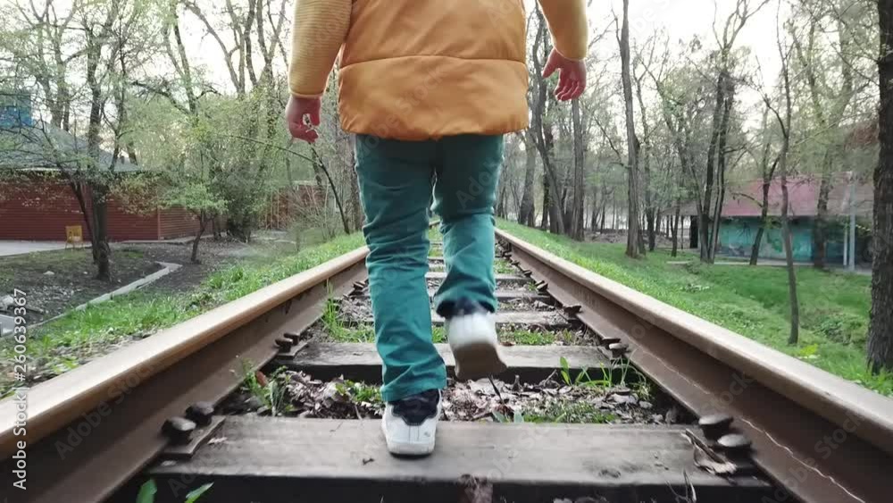 A little boy walks straight along the train tracks railway railroad sleepers A little boy walks straight along the train tracks railway railroad sleepers