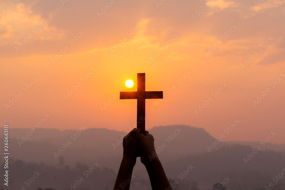 human hands praying to the GOD while holding a crucifix symbol with bright sunbeam on the sky