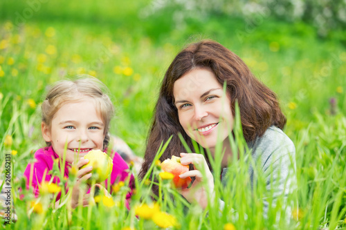 Mother and daughter lying on green meadow and eating apples