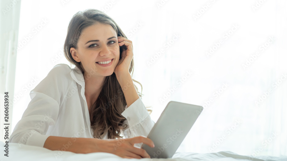 Beautiful cute girl woman holding a smart phone tablet computer in the morning white bedroom - lifestyle female at home Beautiful cute girl woman holding a smart phone tablet computer in the morning white bedroom - lifestyle female at home