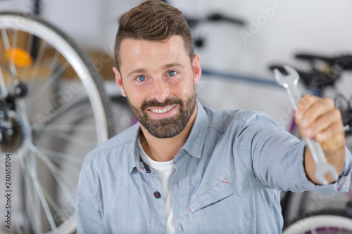 smiling male bike technician showing wrench at the camera