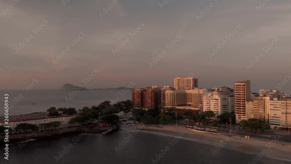 Aerial panning down movement at golden hour at the Copacabana fort in Rio de Janeiro with the ocean waves coming in on the beach, sunlight hitting the buildings and islands in the background Aerial panning down movement at golden hour at the Copacabana fort in Rio de Janeiro with the ocean waves coming in on the beach, sunlight hitting the buildings and islands in the background