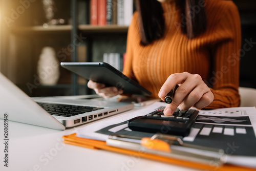 Businesswoman hands working with finances about cost and calculator and laptop with tablet, smartphone at office in morning light