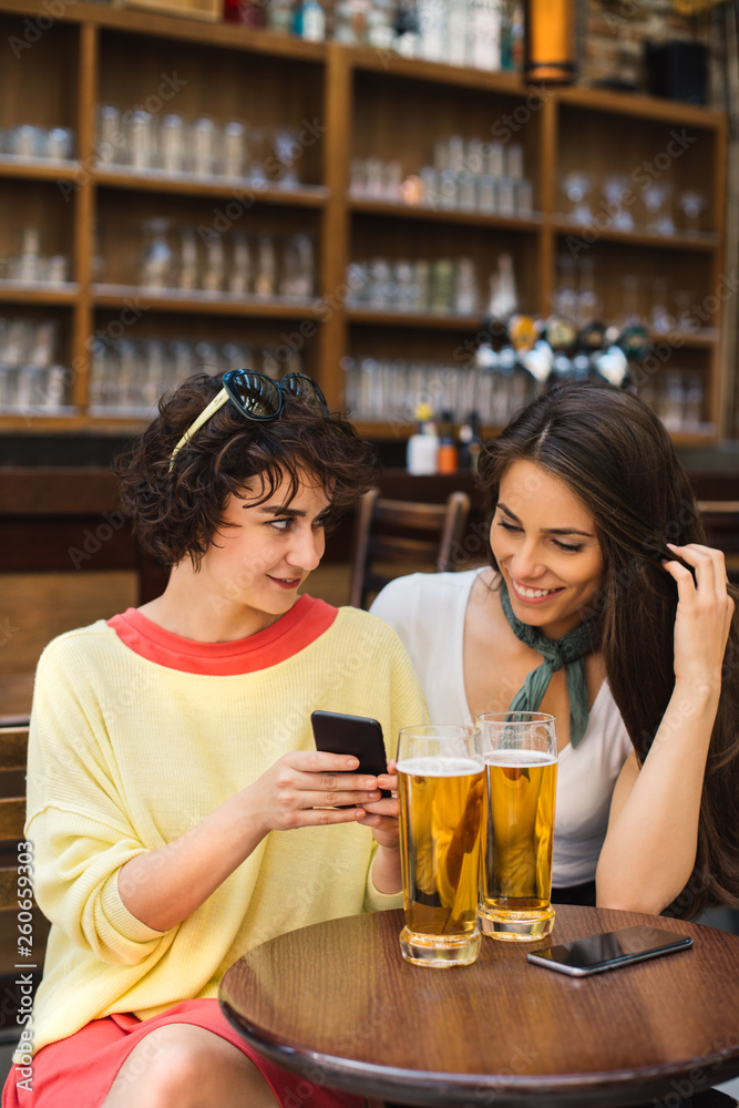 Two girls chatting while having a beer. Long haired and short haired girl drinking beer. Two girls chatting while having a beer. Long haired and short haired girl drinking beer.