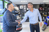 motorcycle dealer shaking hands with customer entering shop