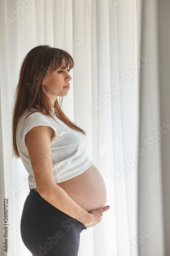Beautiful pregnant woman standing near window.