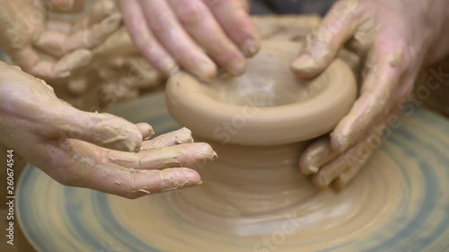 Two intertwined hands form a pot of clay on a potter's wheel. A male hand helps a woman's hands shape a clay shape.
