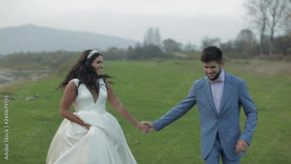 Wedding couple running near mountain river. Groom and bride in love Wedding couple running near mountain river. Groom and bride in love