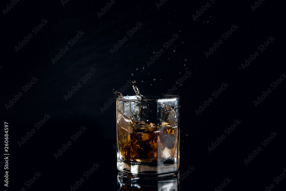Whiskey splash from the fallen ice cube into glass with beverage isolated on black background.. Whiskey splash from the fallen ice cube into glass with beverage isolated on black background..