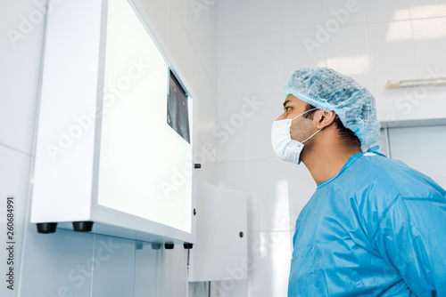side view of doctor in medical cap and latex glove looking at x-ray in clinic