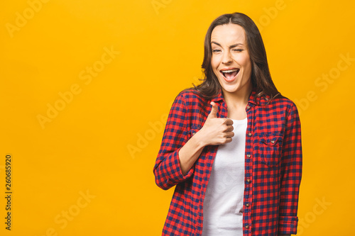 Portrait of a pretty happy woman in casual posing isolated on a yellow background. Thumbs up.