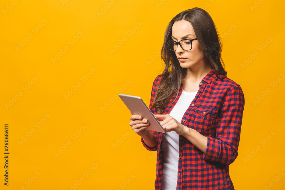 Portrait with copy space empty place of pretty charming confident smiling woman in casual having tablet in hands isolated against yellow background. Portrait with copy space empty place of pretty charming confident smiling woman in casual having tablet in hands isolated against yellow background.