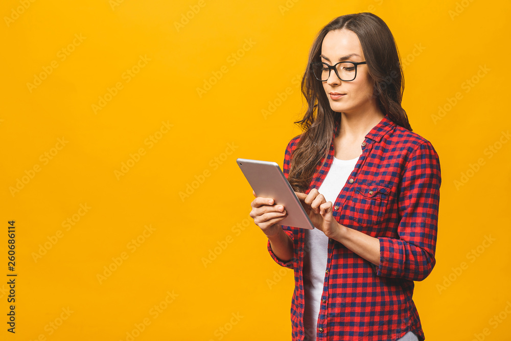 Portrait with copy space empty place of pretty charming confident smiling woman in casual having tablet in hands isolated against yellow background. Portrait with copy space empty place of pretty charming confident smiling woman in casual having tablet in hands isolated against yellow background.