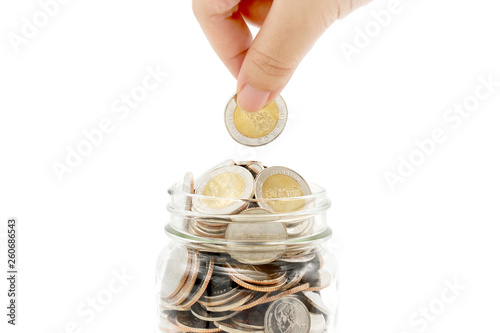 Woman's hand dropping new ten Thai Baht coin into a glass jar full of coins, isolated on white background. Business and finance concept.