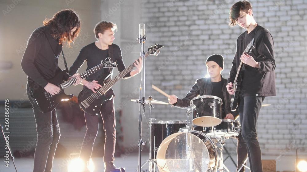 A young rock group having a repetition in a garage. Members of a group wearing black clothes. Bright lighting