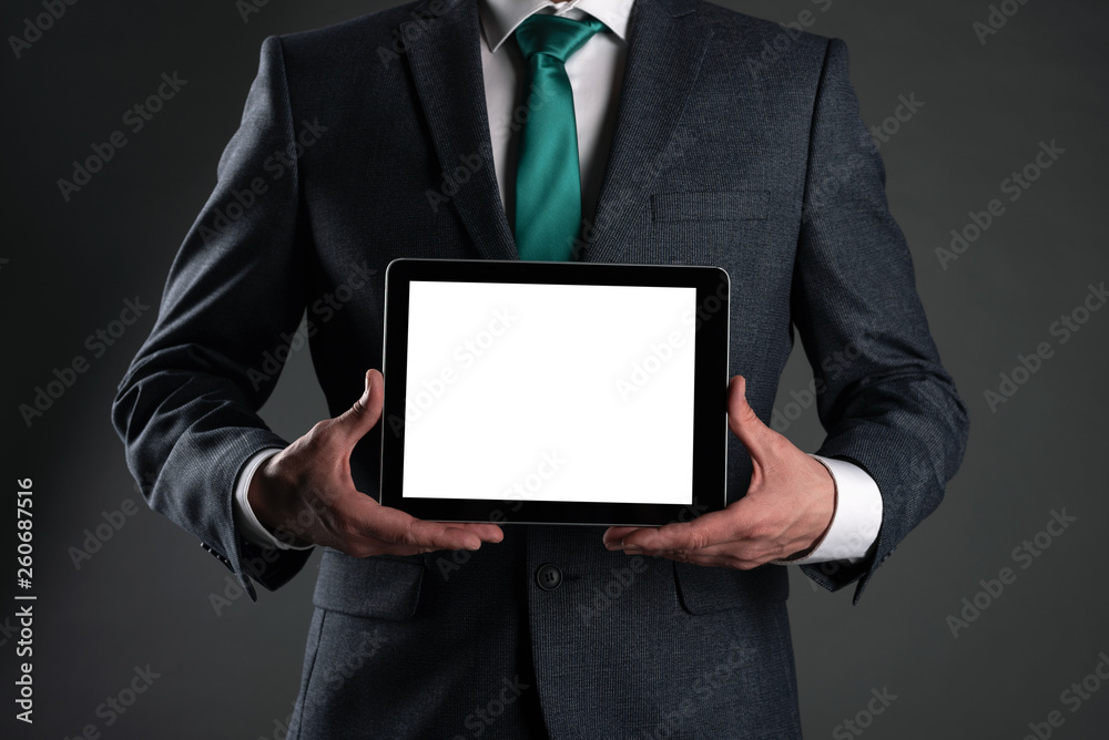 Digital tablet computer with a blank screen in a business man hands on gray background. Special offer mock up. Business proposal template. Contact us phone number background with copy space. Digital tablet computer with a blank screen in a business man hands on gray background. Special offer mock up. Business proposal template. Contact us phone number background with copy space.