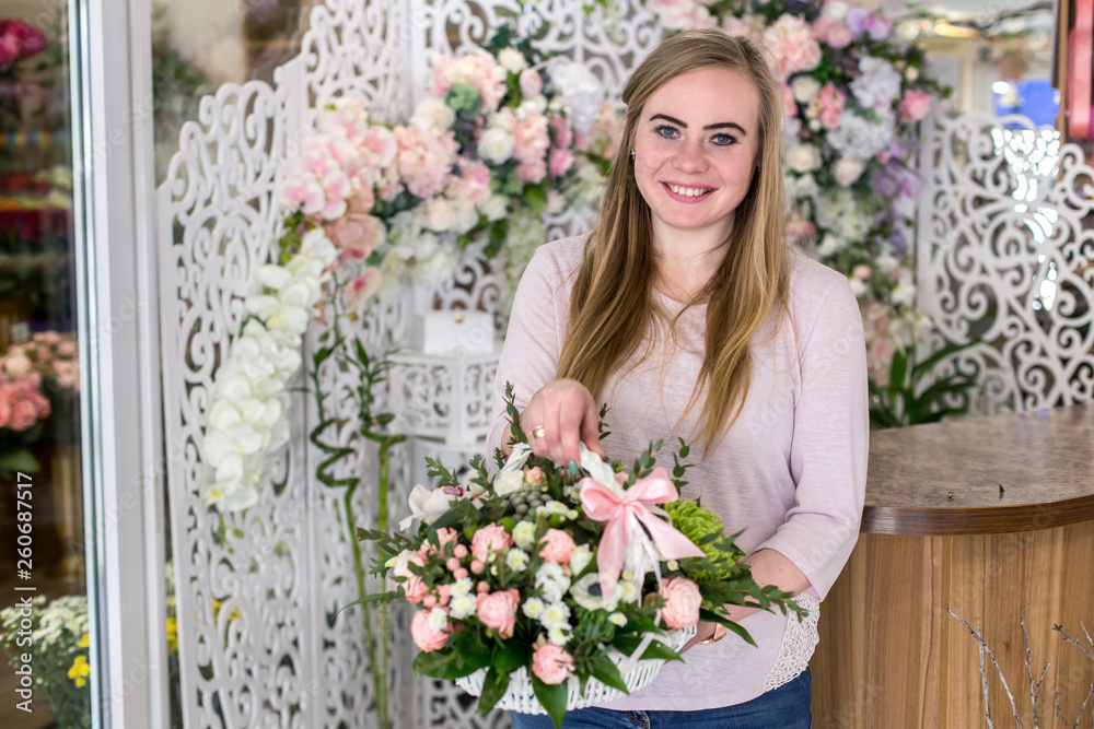 Smiling young florist woman holding a beautiful bouquet of roses in white basket.