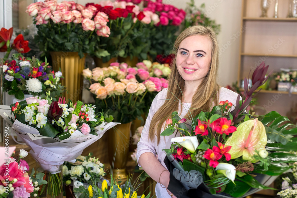 Smiling young florist woman holding a beautiful flower bouquet  in a floral boutique. Looking at camera.