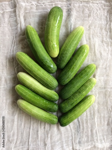 Cucumbers, fresh green leaves arranged in a pattern similar resting on a white cloth.