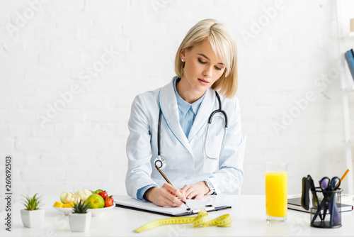 attractive blonde nutritionist in white coat writing on clipboard