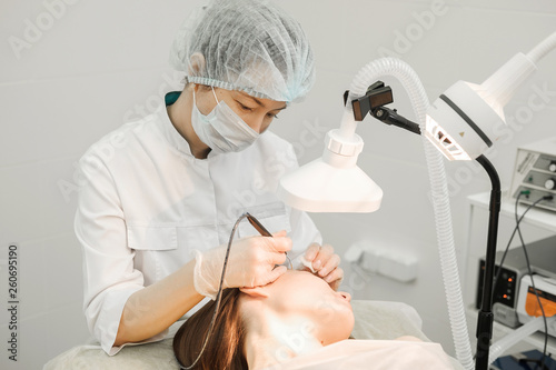 Medical treatment removal of birthmark from female patient's face. Female dermatologist surgeon using a professional electrocautery for removing mole. Radio wave electrocoagulation remove method photo