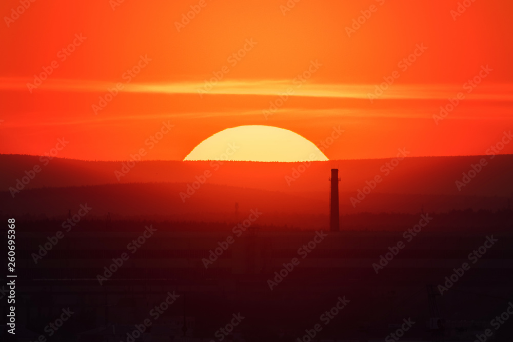 Telephoto lens panoramic shot of cityscape view megalopolis during sunset with giant sun at summer evening