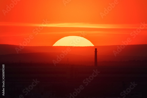 Telephoto lens panoramic shot of cityscape view megalopolis during sunset with giant sun at summer evening © Vasily