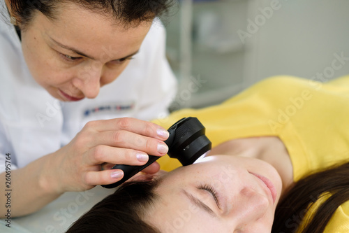 Female dermatologist using a professional dermatoscope while doing skin examination, Checking benign moles on face. Dermatologist examining birthmarks and moles on a female patient. Dermatology Clinic
