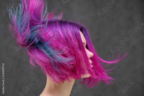 Concept Portrait of a punk girl, young woman with chic purple hair color in studio close up on a colorful background with fluttering hair.