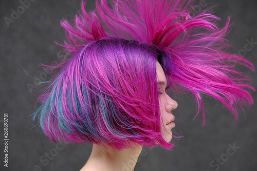 Concept Portrait of a punk girl, young woman with chic purple hair color in studio close up on a colorful background with fluttering hair.