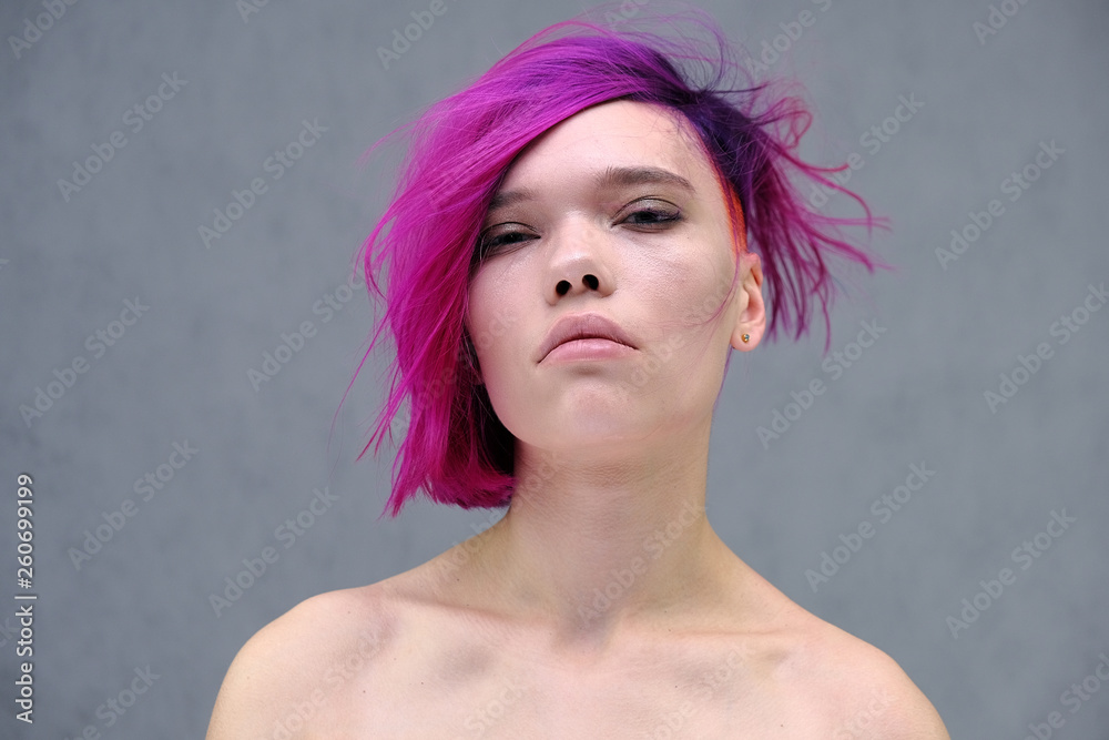 Naklejka premium Concept Portrait of a punk girl, young woman with chic purple hair color in studio close up on a colorful background with fluttering hair.