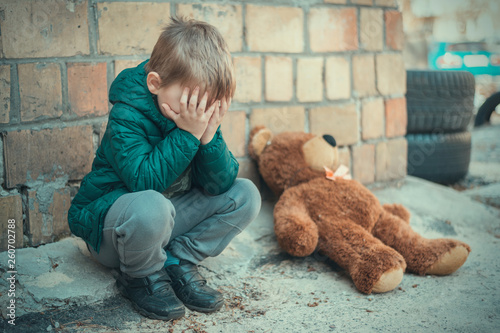 A little boy is crying over a teddy bear outside.