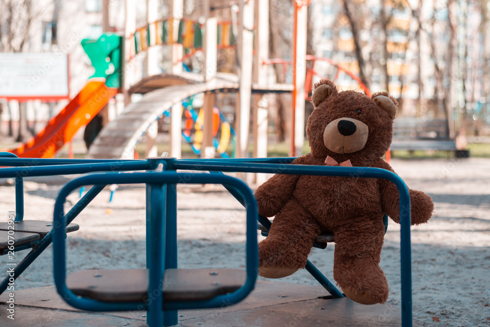 Abandoned teddy bear sitting near the playground.