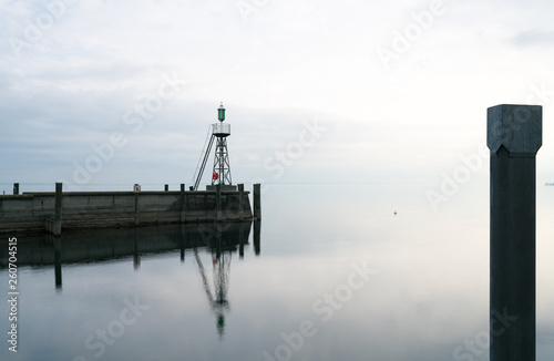 signal light and harbor wall on calm lake waters under an overcast sky negative space abstract