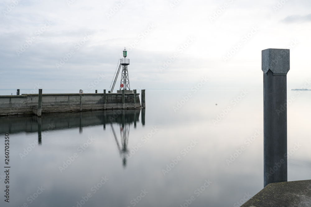 signal light and harbor wall on calm lake waters under an overcast sky negative space abstract