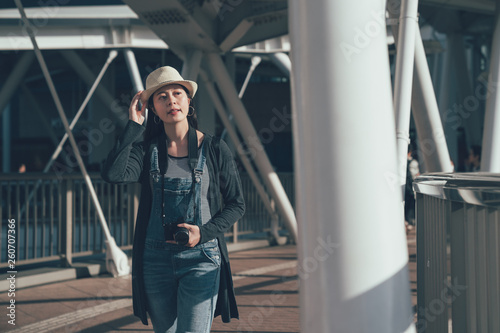 asian smiling elegant woman walking on Footbridge in center of osaka in highest abeno skyscraper in japan. beautiful lady with staw hat carrying camera taking picture while sightseeing city urban. © PR Image Factory