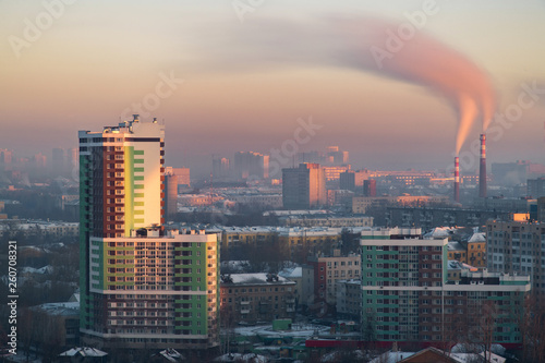 Telephoto lens long exposure with neutral destiny filter shot of morning cityscape during sunrise with pipes and chimney emitting steam