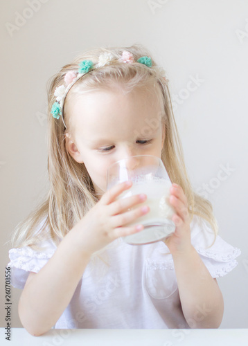 Little blond girl drink a glass of milk with different emotions, indoor, healthy food concept